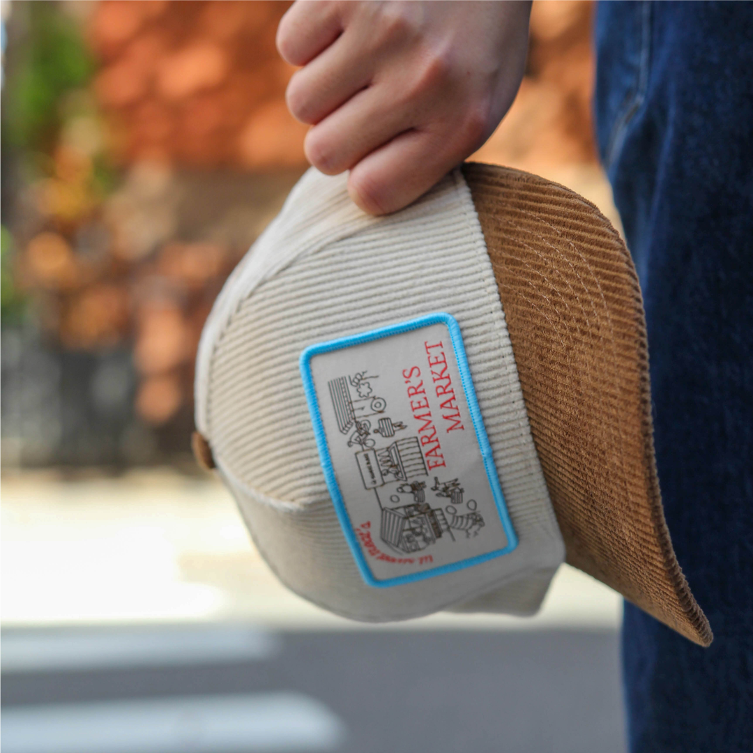 Hand holding a cream and brown product with a 'Farmers Market' label, blurred background