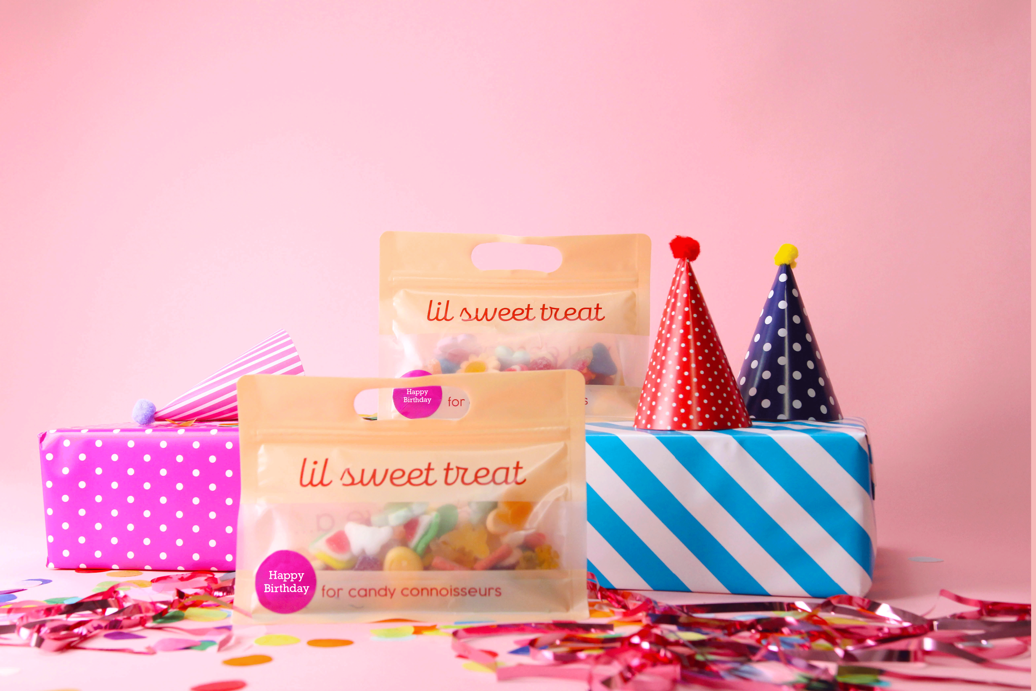 Packages of 'lil sweet treat' candy with colorful party hats and a striped box on a pink background.