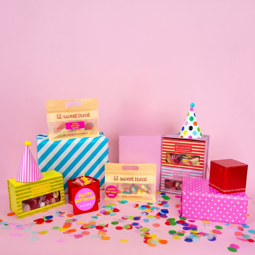 Assorted party favor boxes and decorations on a pink background with confetti.